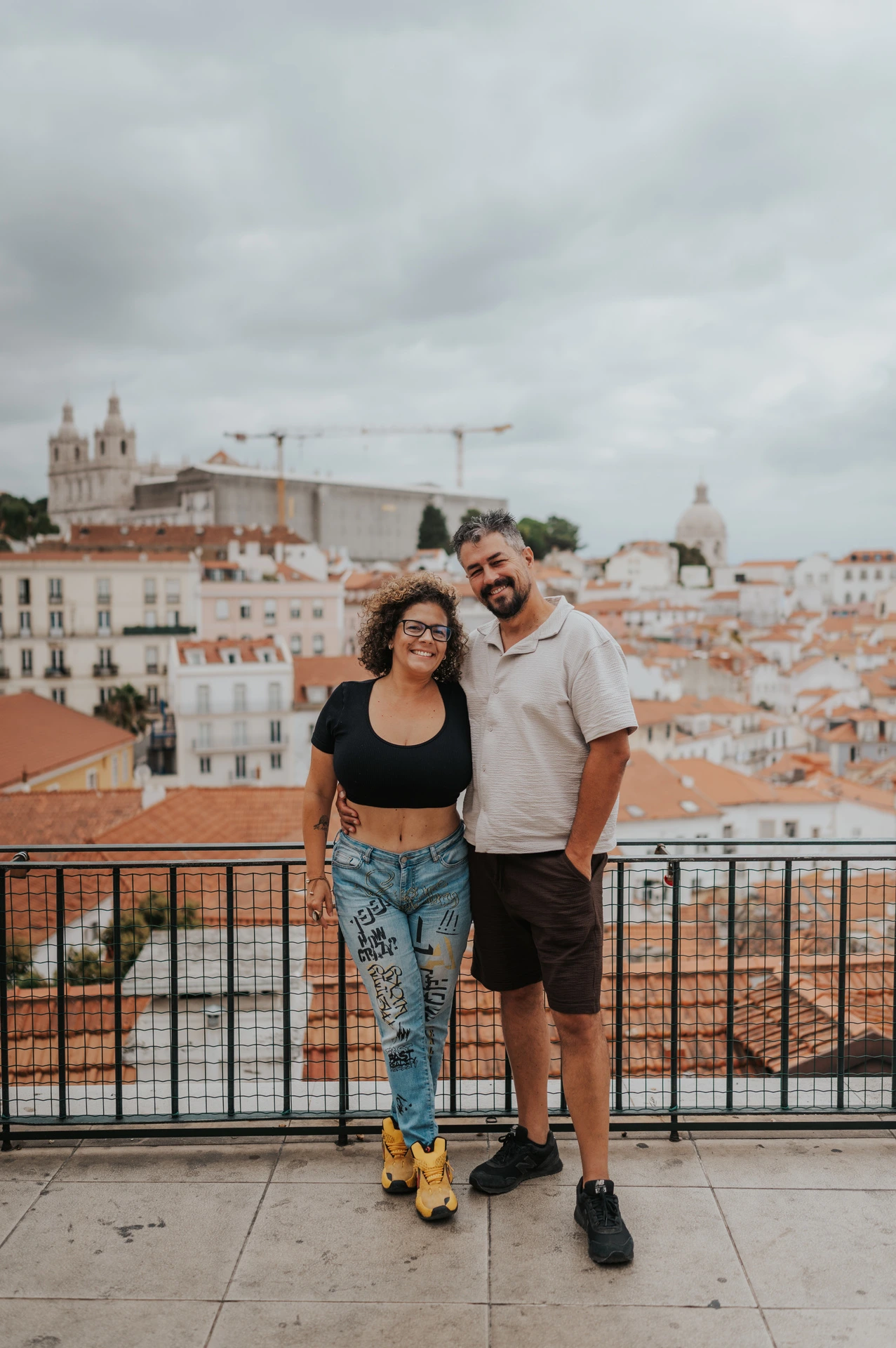 The parents standing close together and smiling beside the viewpoint railing during their family photoshoot in Lisbon.