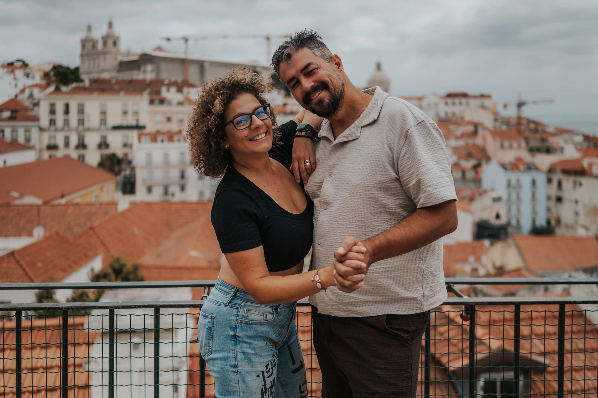 The parents standing close together and smiling beside the viewpoint railing during their family photoshoot in Lisbon.