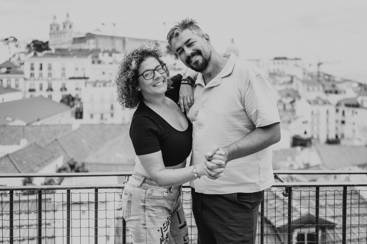 A portrait of the parents above the city in black and white | Lisbon family photoshoot Black-and-white photograph: the parents standing close together and smiling beside the viewpoint railing during their family photoshoot in Lisbon.