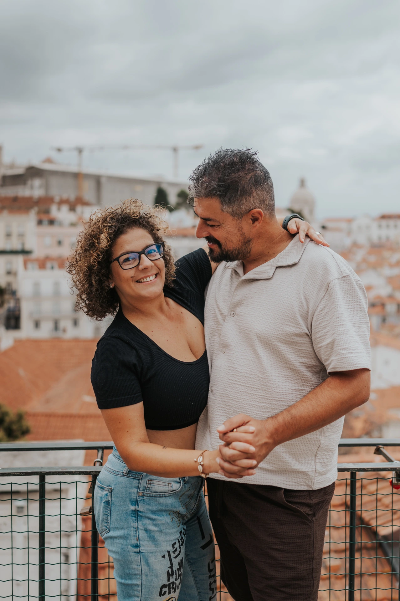 The parents standing close together and smiling beside the viewpoint railing during their family photoshoot in Lisbon.