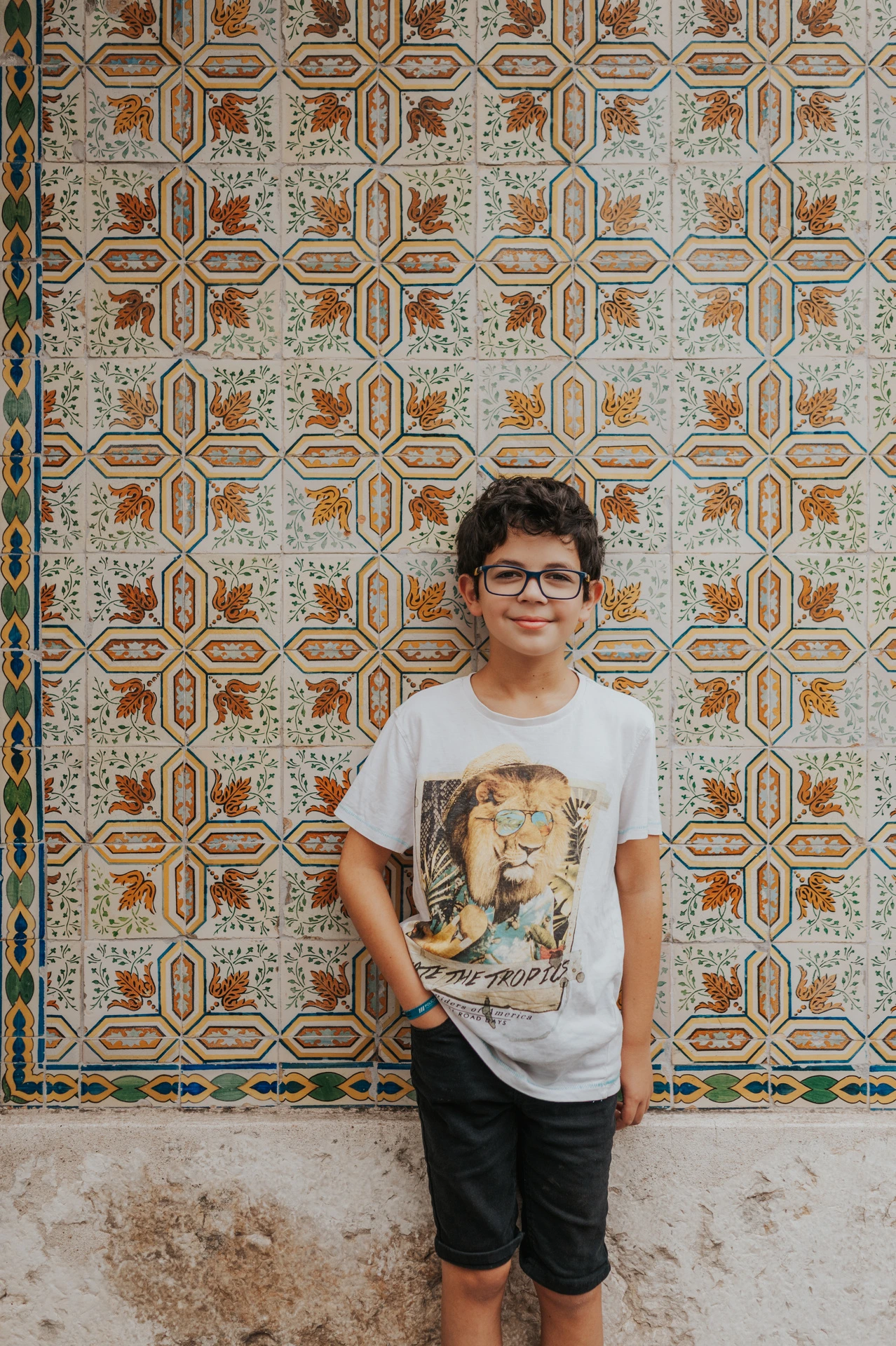 The younger child standing in front of a colourful patterned tile panel during their family photoshoot in Lisbon.