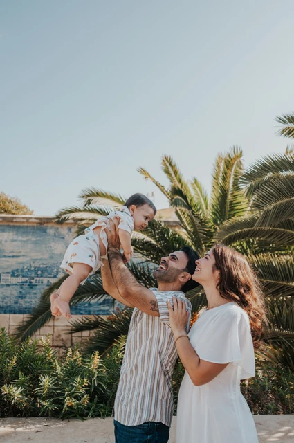 A playful lift beside the palms | Lisbon family photoshoot The parents lifting their smiling child between them beside palms and blue tiles during their family photoshoot in Lisbon.