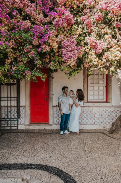 The family standing together at a red doorway beneath flowering branches during their family photoshoot in Lisbon.