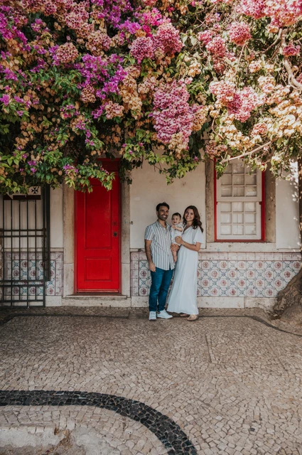 Together beneath the flowering doorway | Lisbon family photoshoot The family standing together at a red doorway beneath flowering branches during their family photoshoot in Lisbon.