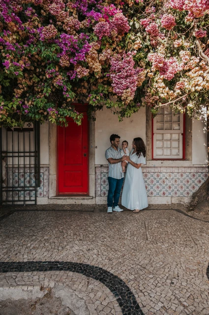 Together beneath the flowering doorway | Lisbon family photoshoot The family standing together at a red doorway beneath flowering branches during their family photoshoot in Lisbon.