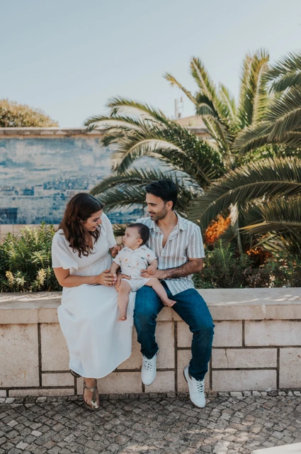 Seated together beside the viewpoint palms | Lisbon family photoshoot The parents seated together with their one-year-old child beside palms and blue Portuguese tiles during their family photoshoot in Lisbon.