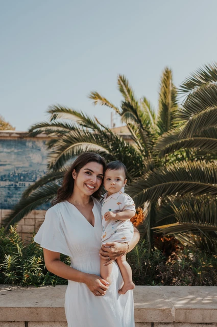 A mother-and-child portrait beside the palms | Lisbon family photoshoot The mother holding her child close beside the palms and blue tile wall during their family photoshoot in Lisbon.