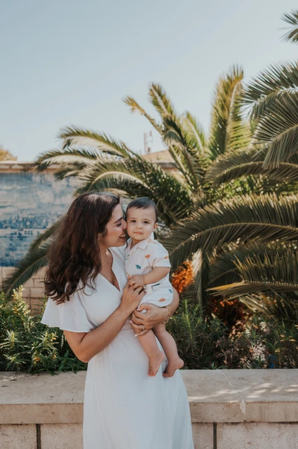 A mother-and-child portrait beside the palms | Lisbon family photoshoot The mother holding her child close beside the palms and blue tile wall during their family photoshoot in Lisbon.