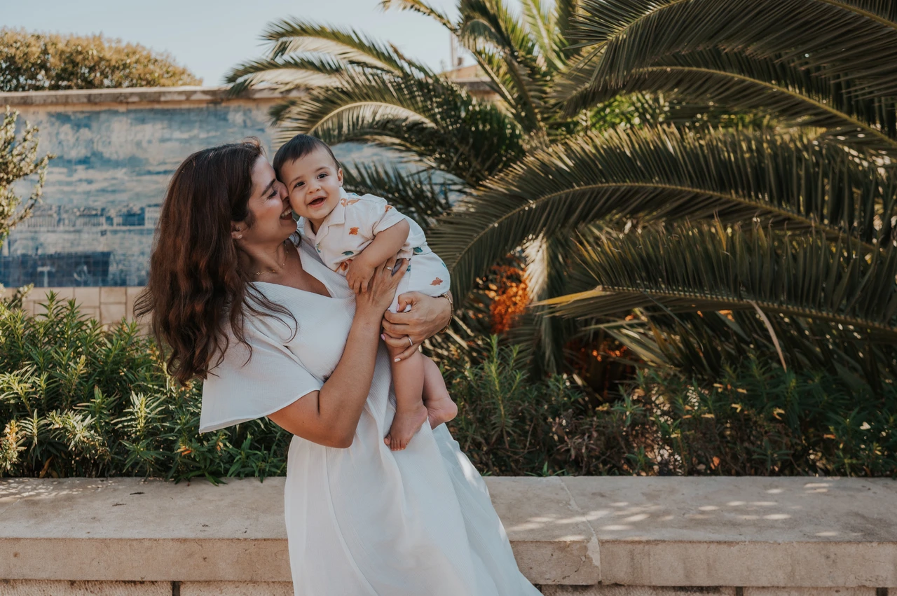 A mother-and-child portrait beside the palms | Lisbon family photoshoot The mother holding her child close beside the palms and blue tile wall during their family photoshoot in Lisbon.