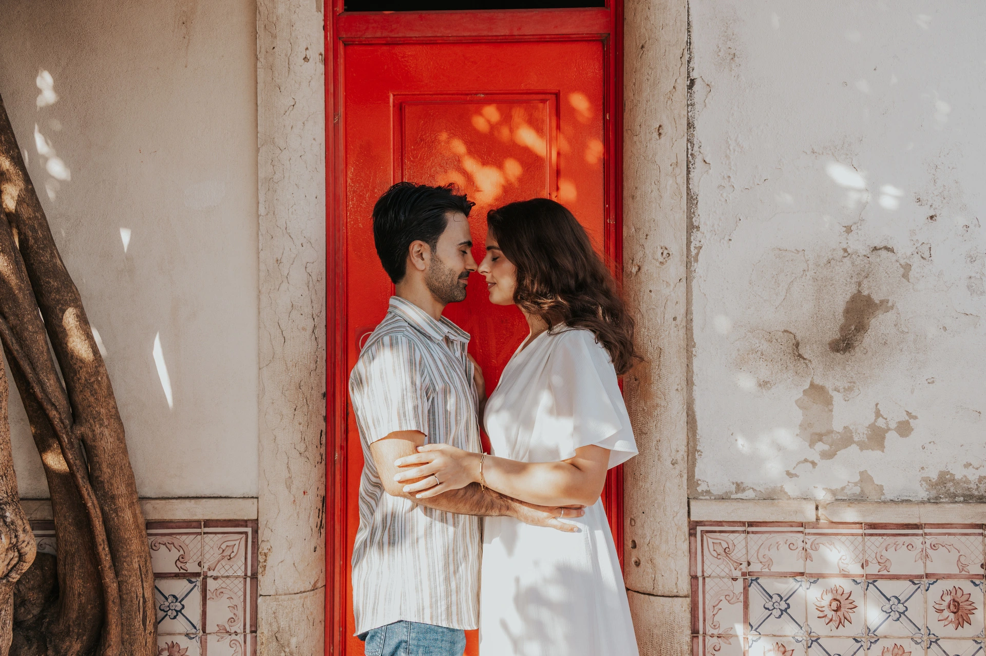 The parents standing close together and facing each other beside the red doorway during their family photoshoot in Lisbon.