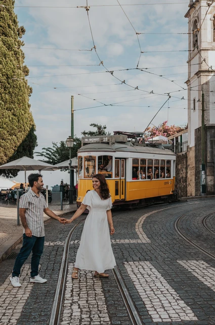 The parents holding hands beside a Lisbon street with a yellow tram behind them during their family photoshoot in Lisbon.