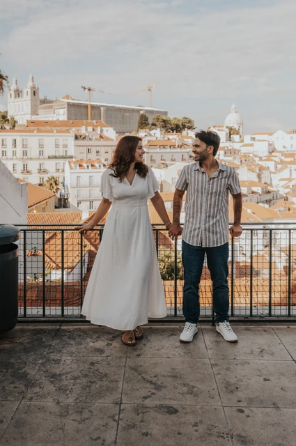 Joined hands above the city | Lisbon family photoshoot The parents holding hands beside the viewpoint railing with the city behind them during their family photoshoot in Lisbon.