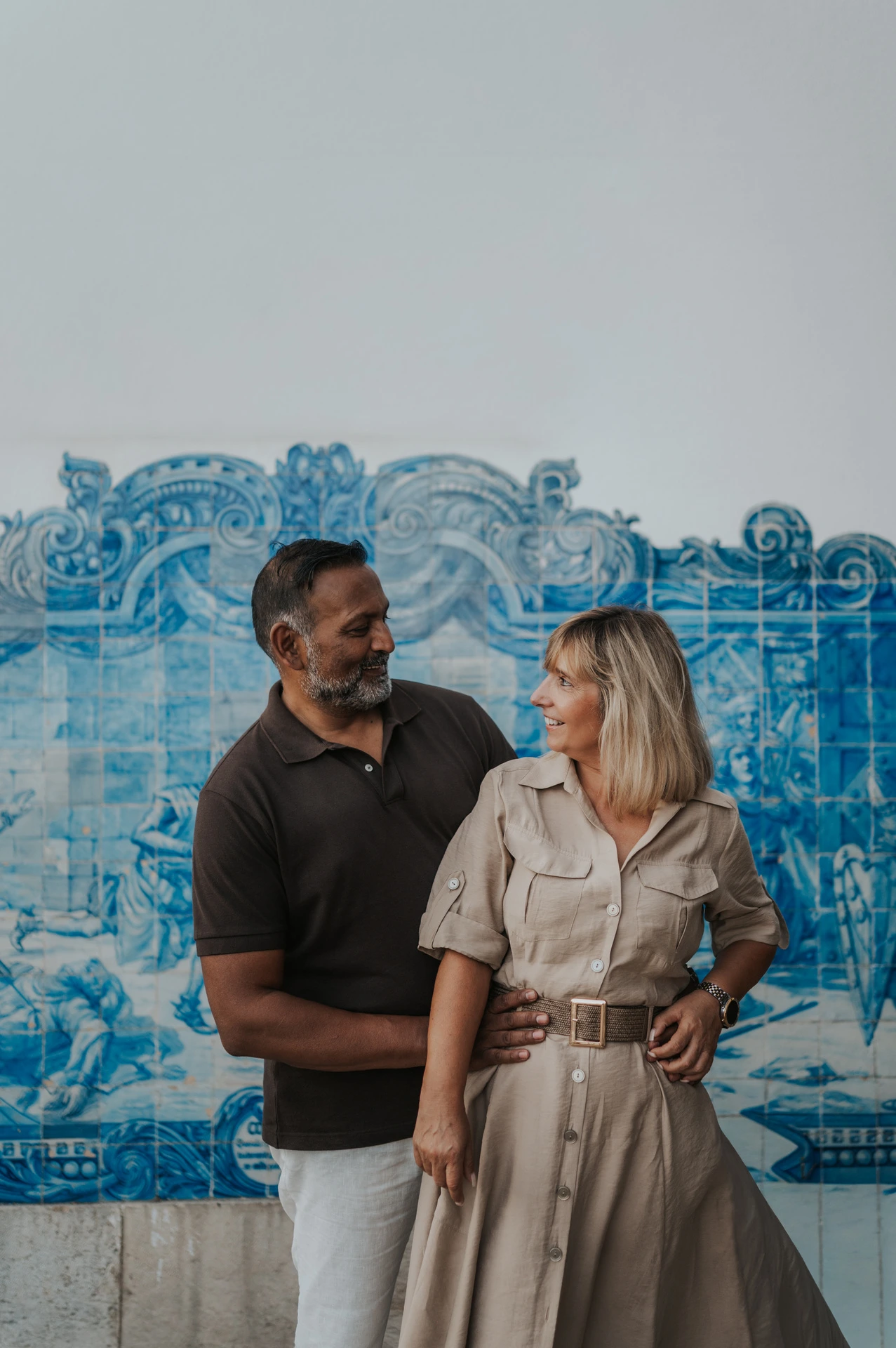 The couple standing close together and smiling at each other in front of the blue tile panel during their couple photoshoot in Lisbon.