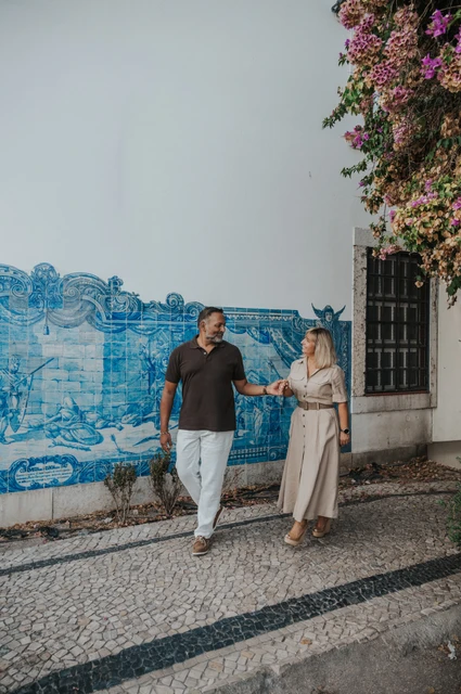 Hand in hand beside the blue tile panel | Lisbon couple photoshoot The couple holding hands in front of a large blue-and-white Portuguese tile panel during their couple photoshoot in Lisbon.