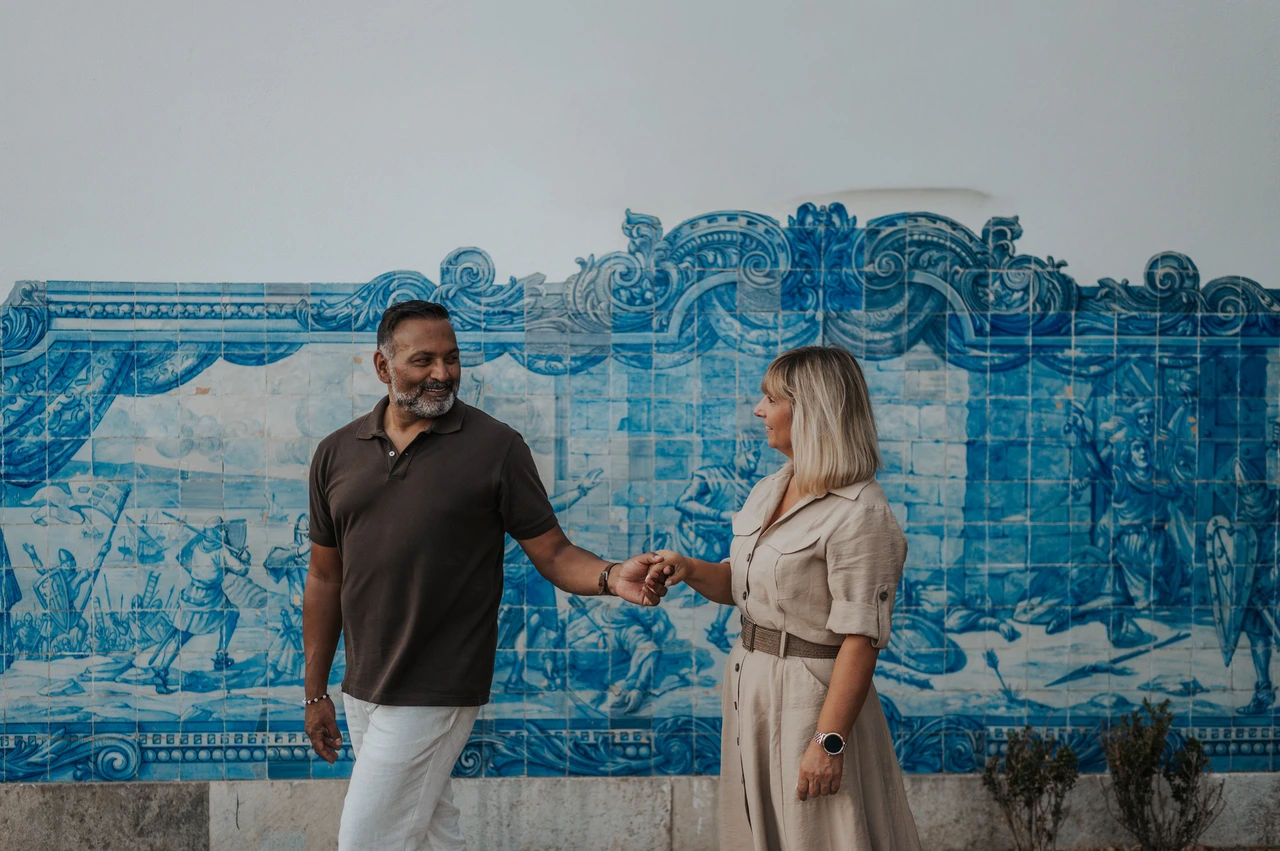 Hand in hand beside the blue tile panel | Lisbon couple photoshoot The couple holding hands in front of a large blue-and-white Portuguese tile panel during their couple photoshoot in Lisbon.