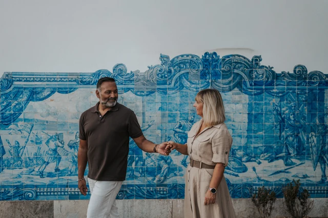 The couple holding hands in front of a large blue-and-white Portuguese tile panel during their couple photoshoot in Lisbon.