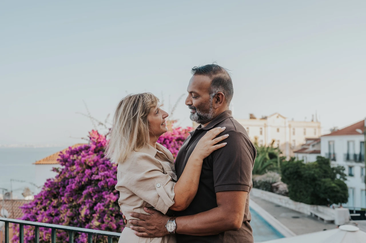 An embrace beside the flowering viewpoint | Lisbon couple photoshoot The couple embracing beside purple flowers with the city and water in the distance during their couple photoshoot in Lisbon.