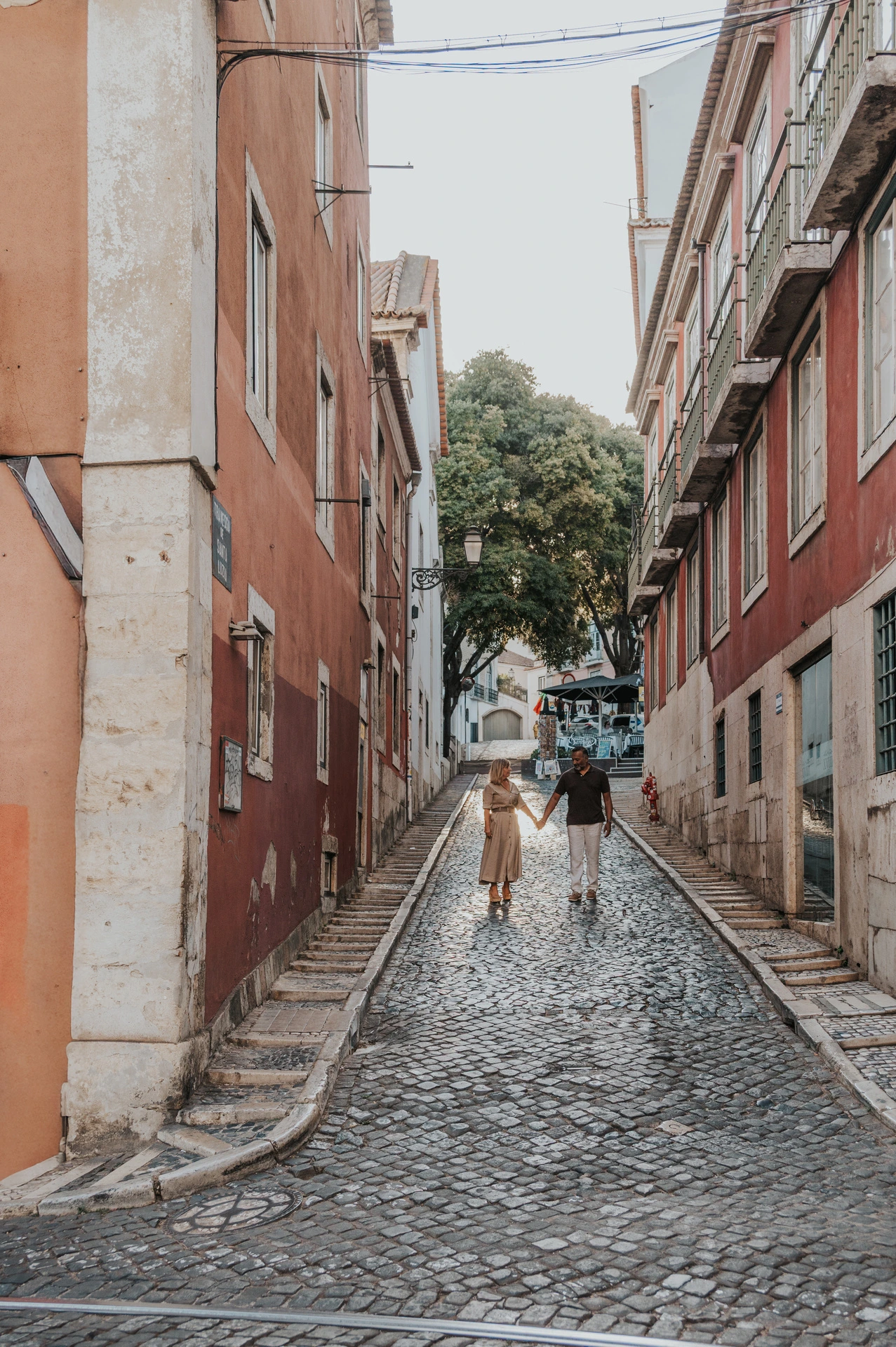 A wide view of the couple walking along a narrow cobbled Lisbon street during their couple photoshoot in Lisbon.