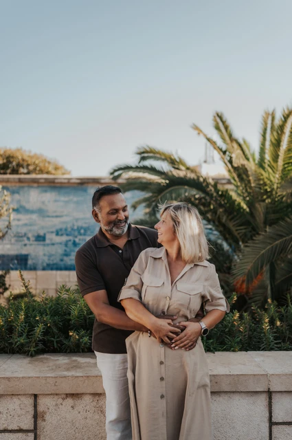 A smiling embrace beside the palms | Lisbon couple photoshoot The man embracing his smiling partner from behind beside palms and blue tiles during their couple photoshoot in Lisbon.