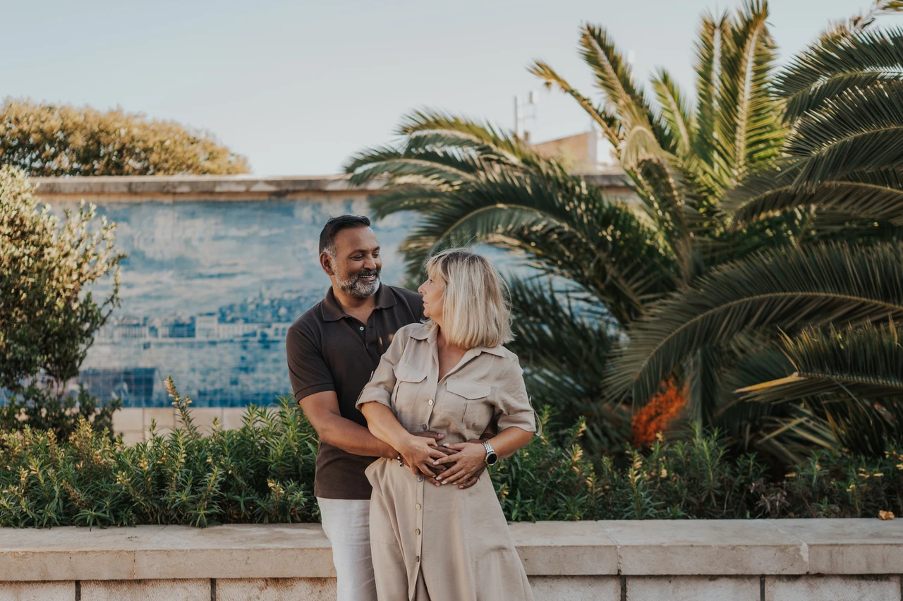 A smiling embrace beside the palms | Lisbon couple photoshoot The man embracing his smiling partner from behind beside palms and blue tiles during their couple photoshoot in Lisbon.