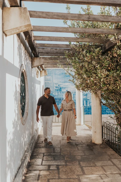 Hand in hand beneath the pergola | Lisbon couple photoshoot The couple walking hand in hand beneath the pergola at Miradouro de Santa Luzia during their couple photoshoot in Lisbon.