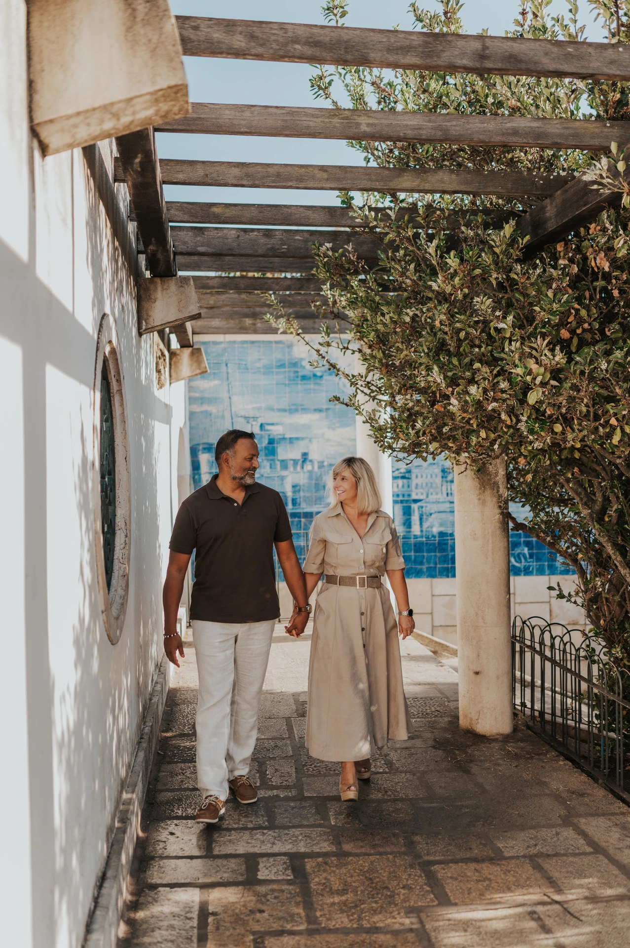 The couple walking hand in hand beneath the pergola at Miradouro de Santa Luzia during their couple photoshoot in Lisbon.