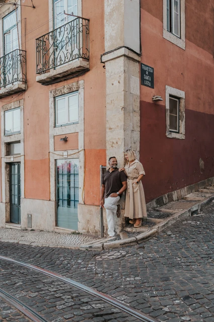Hand in hand at the red street corner | Lisbon couple photoshoot The couple holding hands beside the corner of a red building on a cobbled street during their couple photoshoot in Lisbon.