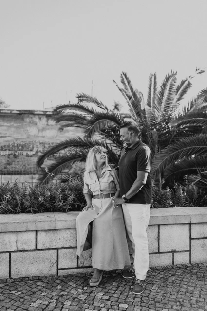 A close portrait at the tiled viewpoint in black and white | Lisbon couple photoshoot Black-and-white photograph: the woman seated on the low wall with her partner standing close beside her by the tiled viewpoint during their couple photoshoot in Lisbon.