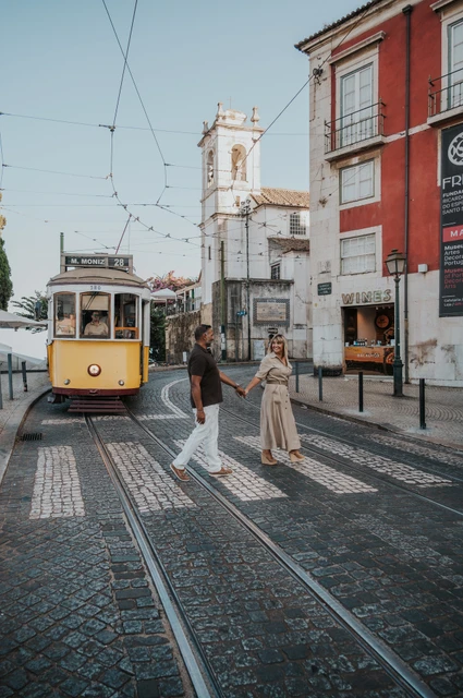 A street portrait with a yellow tram | Lisbon couple photoshoot The couple standing together beside a Lisbon street with a yellow tram behind them during their couple photoshoot in Lisbon.