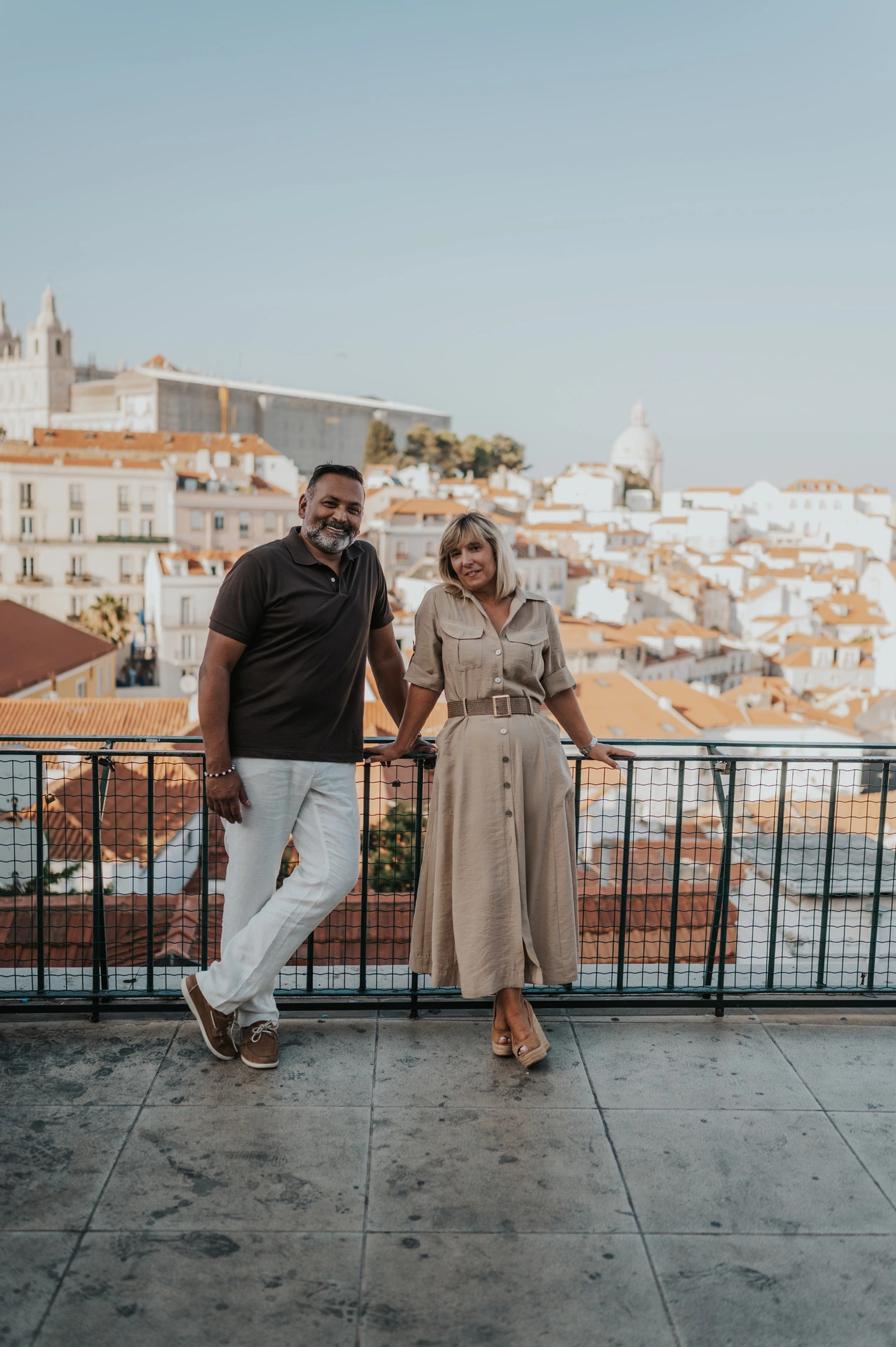 The couple smiling at each other beside the viewpoint railing with Lisbon’s rooftops behind them during their couple photoshoot in Lisbon.