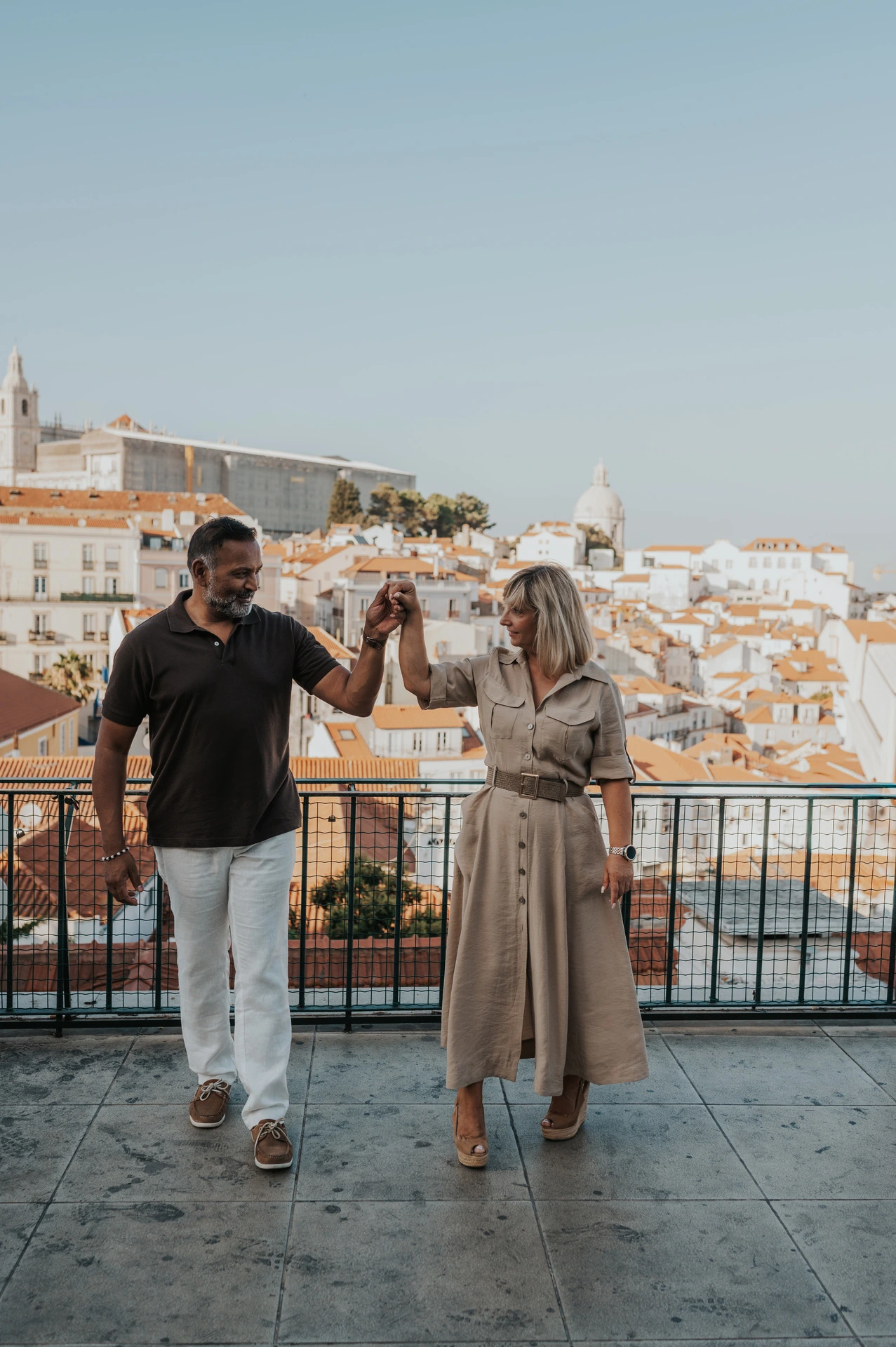 The couple raising their joined hands as she turns beside the viewpoint railing during their couple photoshoot in Lisbon.