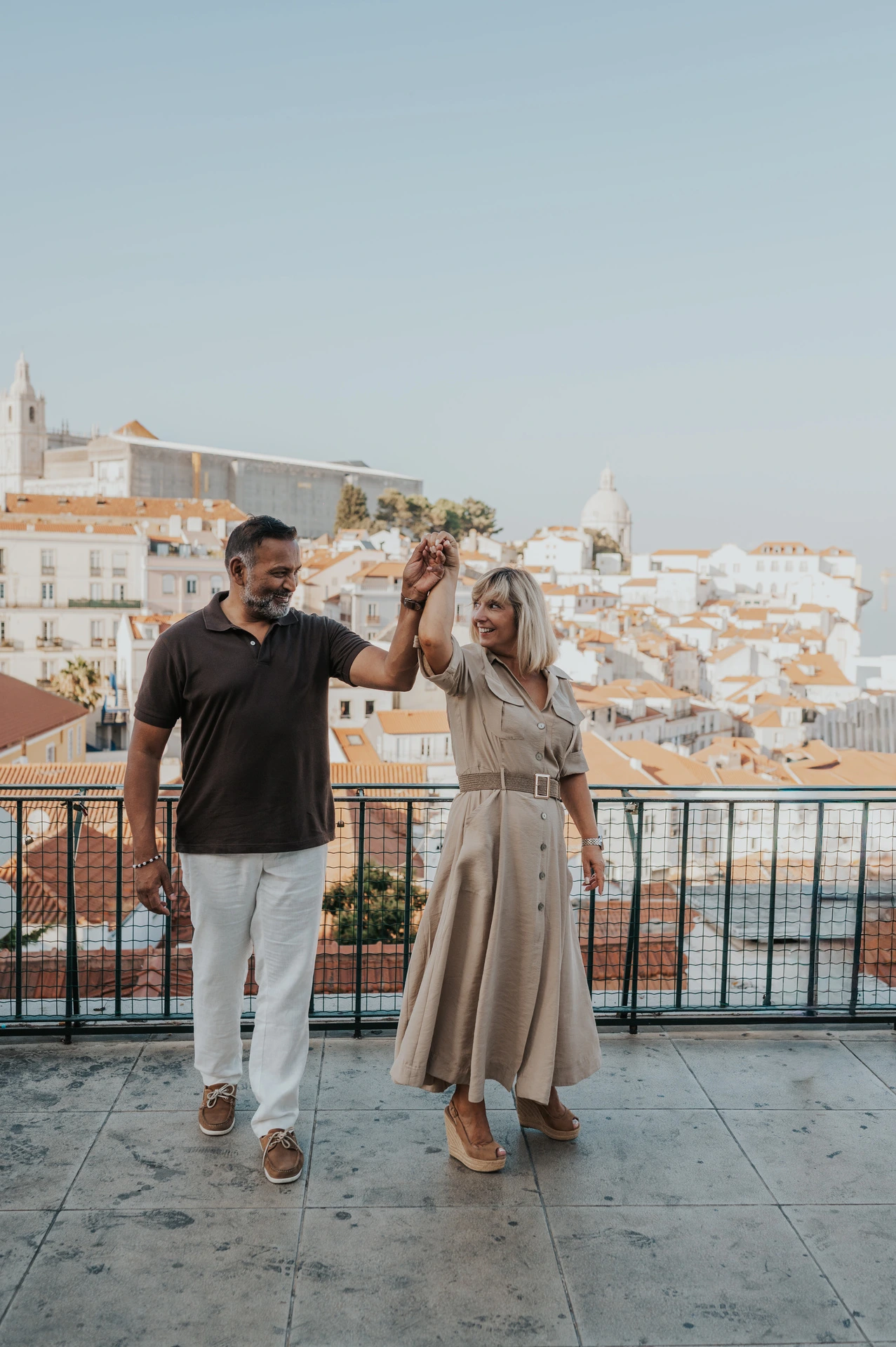 The couple raising their joined hands as she turns beside the viewpoint railing during their couple photoshoot in Lisbon.