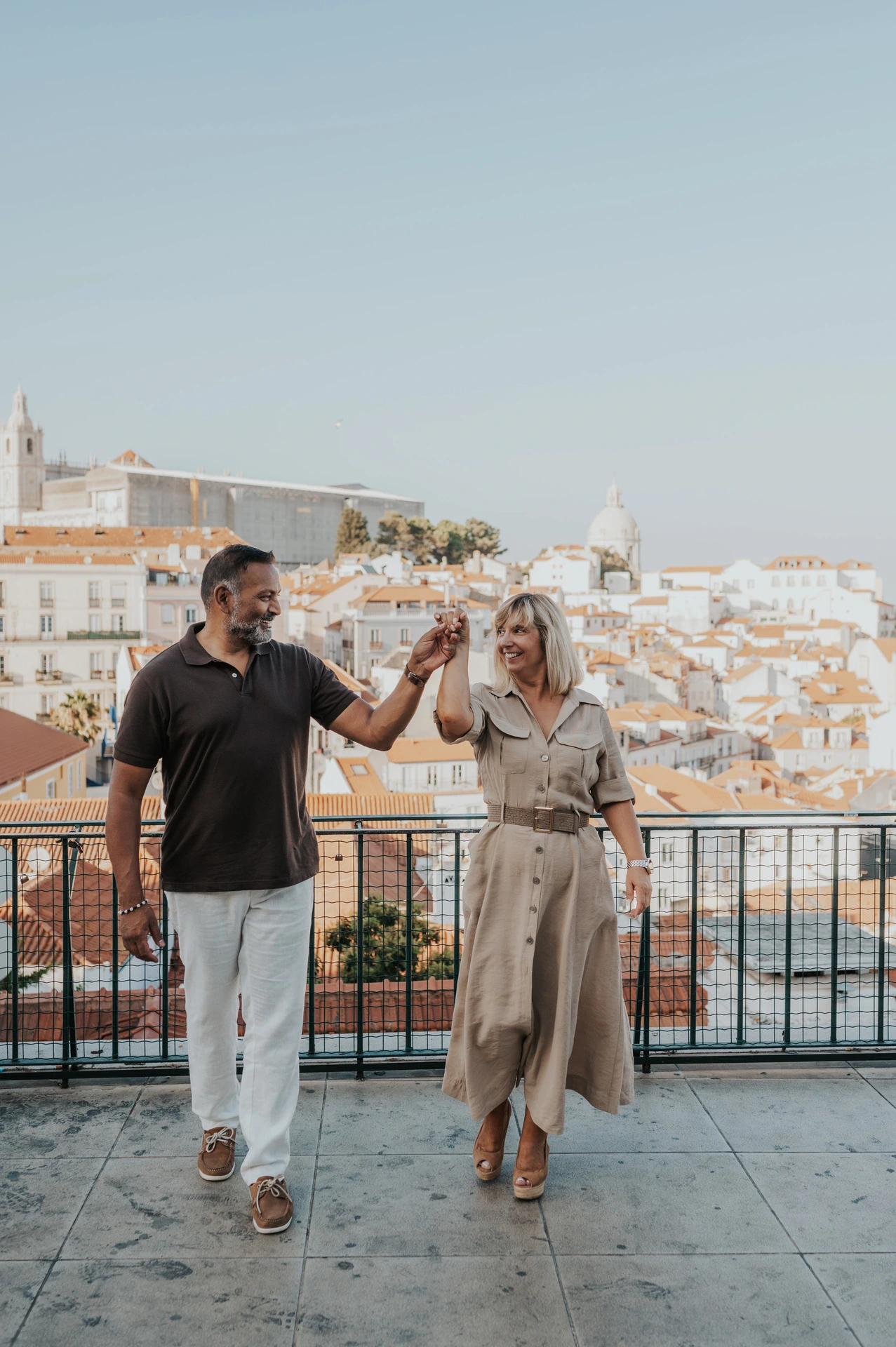 The couple raising their joined hands as she turns beside the viewpoint railing during their couple photoshoot in Lisbon.
