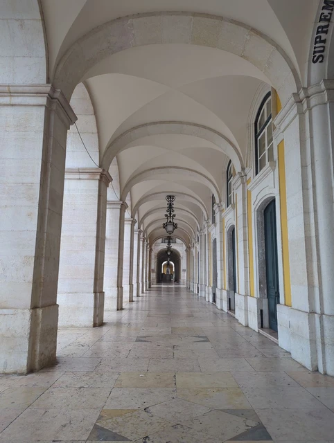 Repeating stone arches and hanging lamps along Praça do Comércio in Lisbon