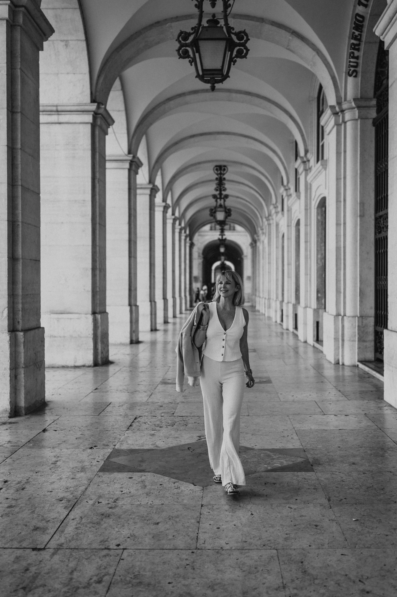 A black-and-white portrait of the woman walking beneath the arcade at Praça do Comércio during her solo photoshoot in Lisbon.