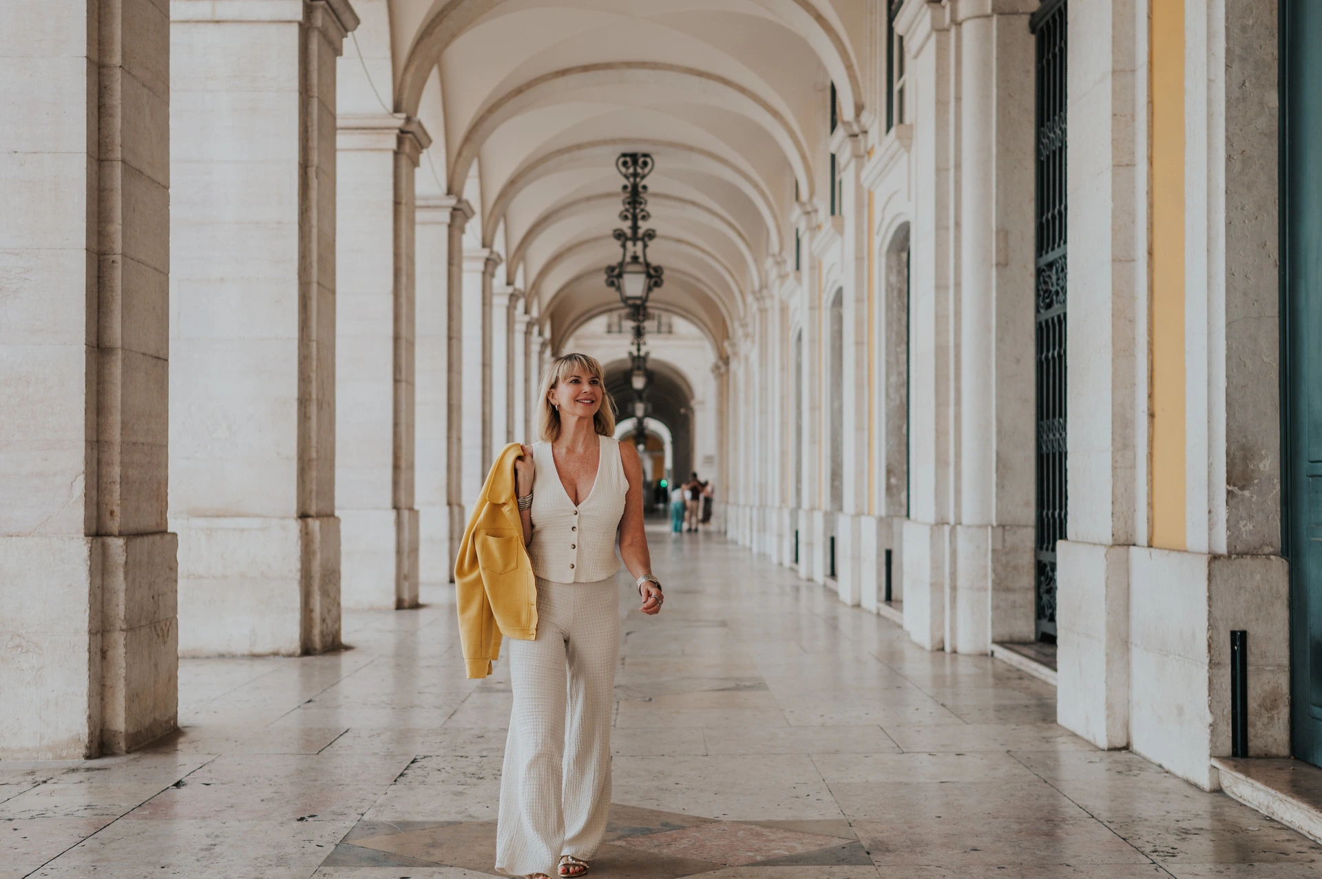The woman smiling as she walks towards the camera beneath the Praça do Comércio arcade during her solo photoshoot in Lisbon.
