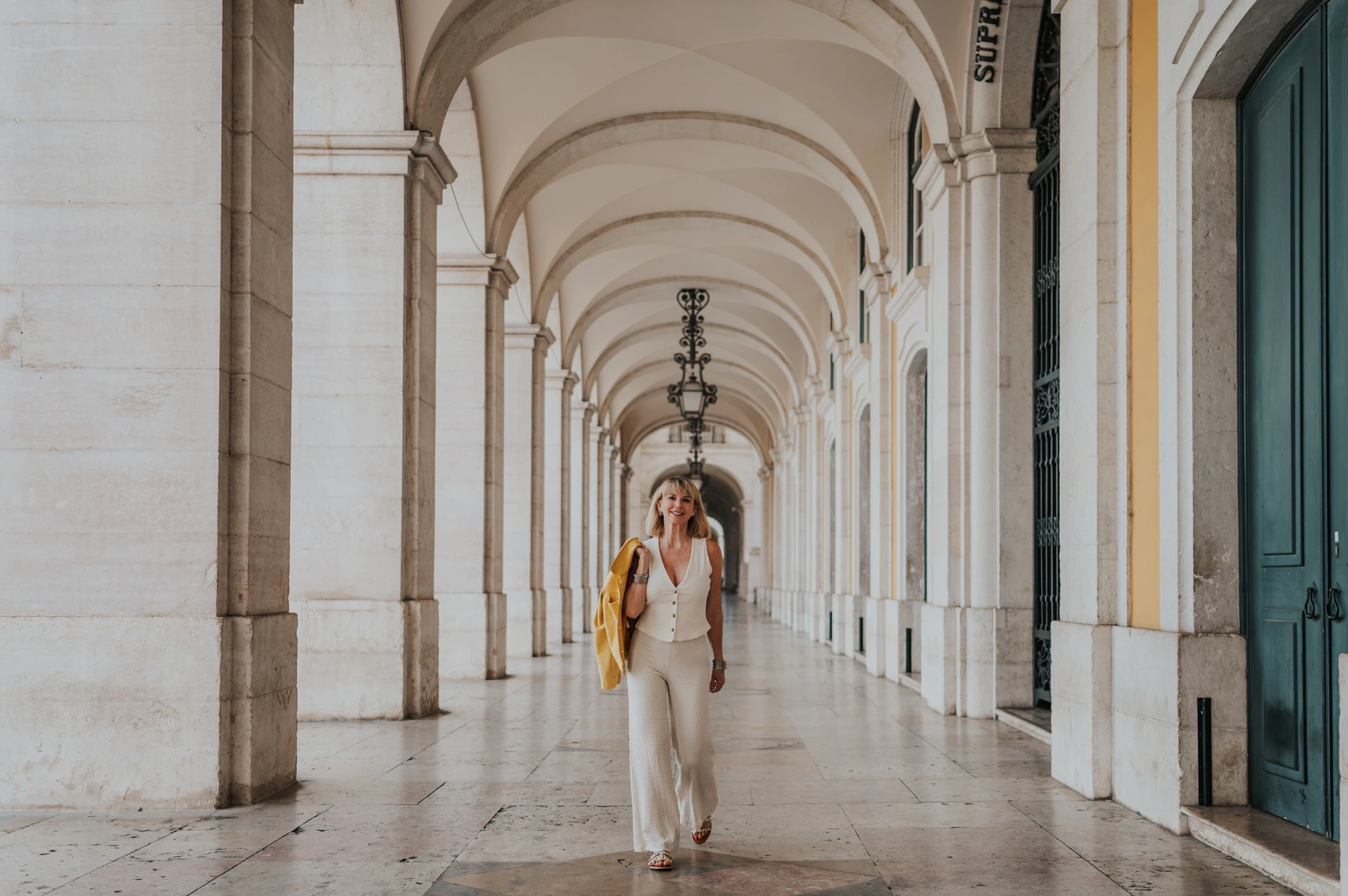 A wide portrait beneath the arcade | Lisbon solo photoshoot A wide photograph of the woman beneath the stone arches at Praça do Comércio during her solo photoshoot in Lisbon.