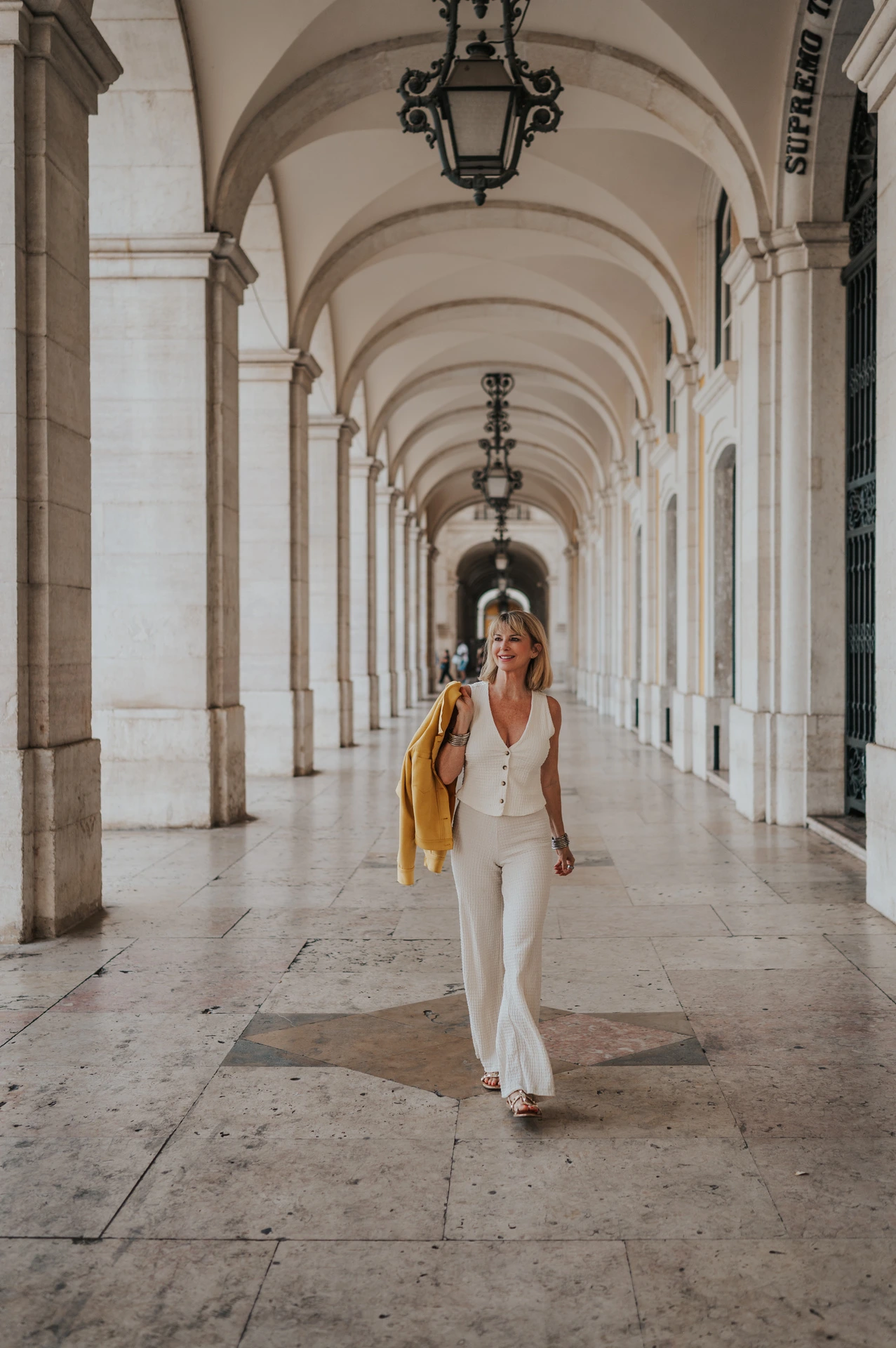 The woman walking towards the camera through the long arcade at Praça do Comércio during her solo photoshoot in Lisbon.