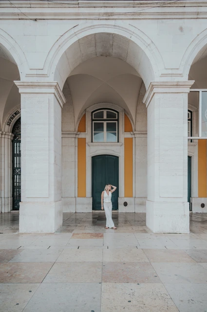 A portrait beneath Praça do Comércio’s arches | Lisbon solo photoshoot The woman with a hand raised to her hair beneath a tall arch at Praça do Comércio during her solo photoshoot in Lisbon.
