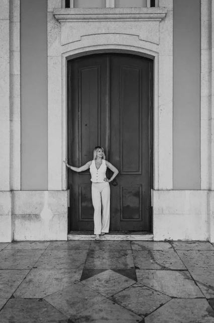 A doorway portrait in black and white | Lisbon solo photoshoot A black-and-white full-length portrait of the woman in front of a tall door at Praça do Comércio during her solo photoshoot in Lisbon.