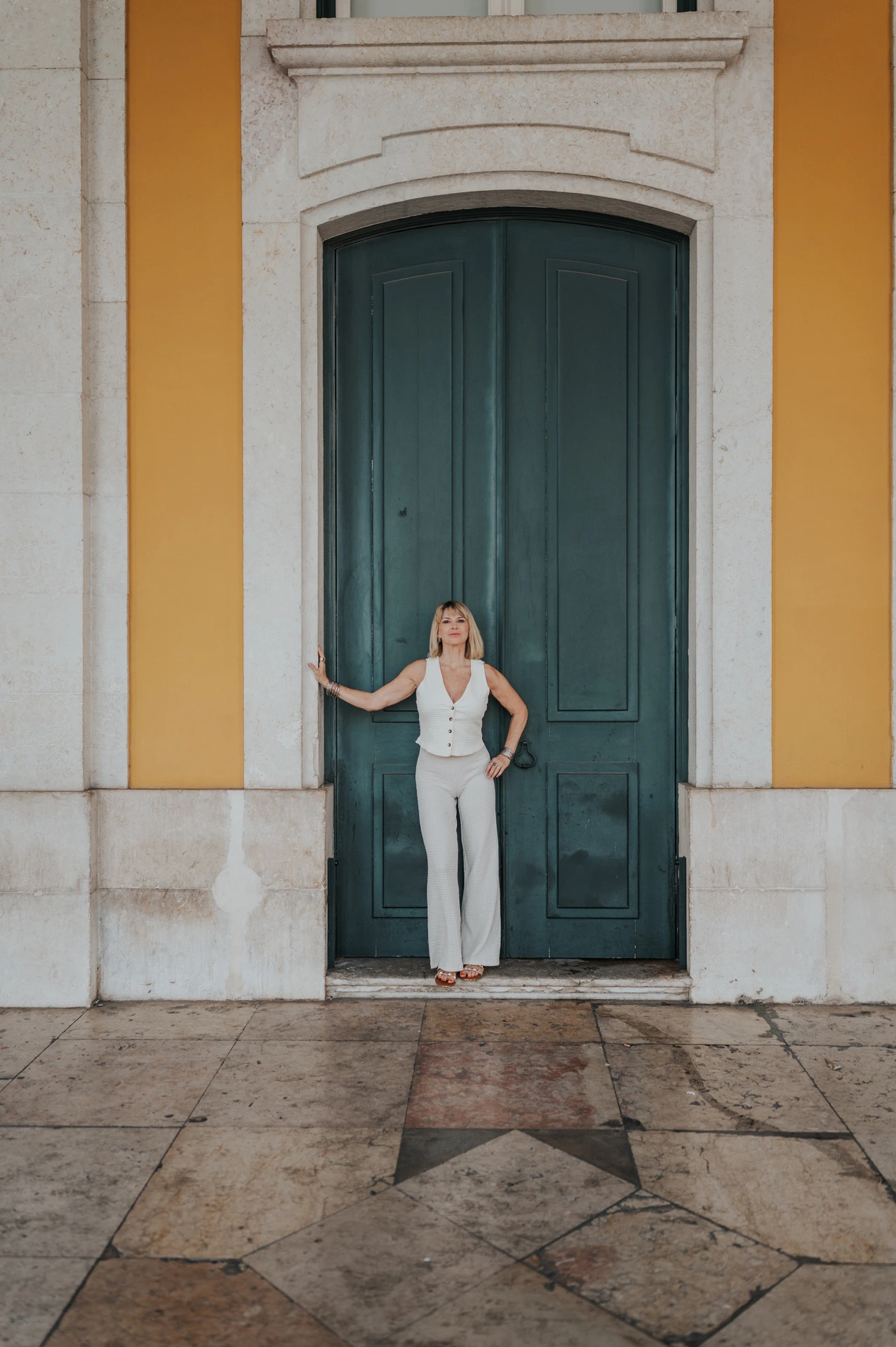 The woman standing with one hand on a tall green door framed by yellow walls at Praça do Comércio during her solo photoshoot in Lisbon.