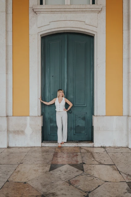 A full-length portrait of the woman in front of the green door and yellow facade at Praça do Comércio during her solo photoshoot in Lisbon.