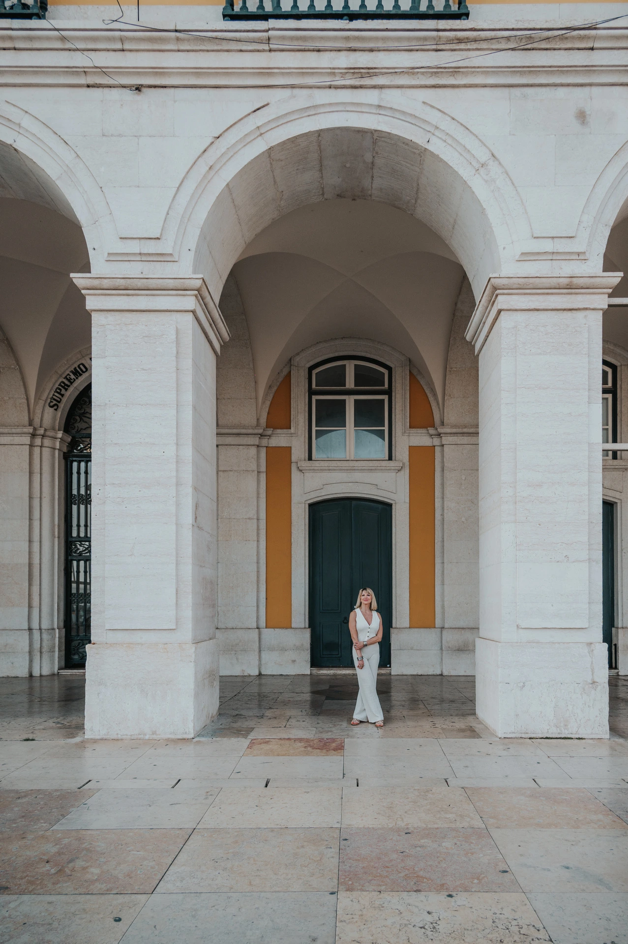 The woman framed beneath a tall stone arch with a green door behind her at Praça do Comércio during her solo photoshoot in Lisbon.