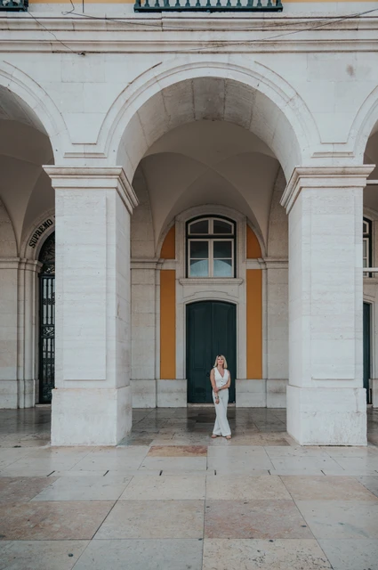 Framed by a grand Praça do Comércio arch | Lisbon solo photoshoot The woman framed beneath a tall stone arch with a green door behind her at Praça do Comércio during her solo photoshoot in Lisbon.