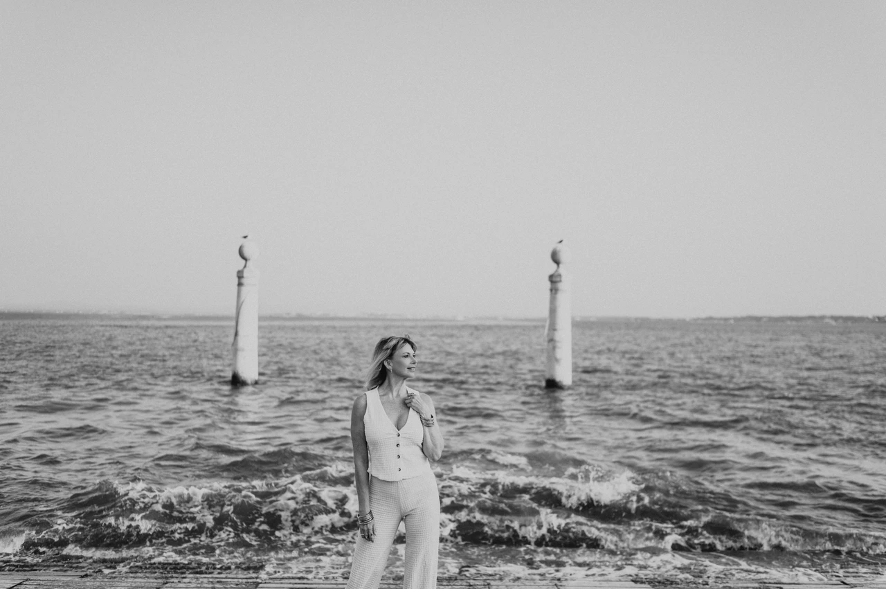 The waterfront waves in black and white | Lisbon solo photoshoot A black-and-white photograph of the woman beside the waves and waterfront columns near Praça do Comércio during her solo photoshoot in Lisbon.