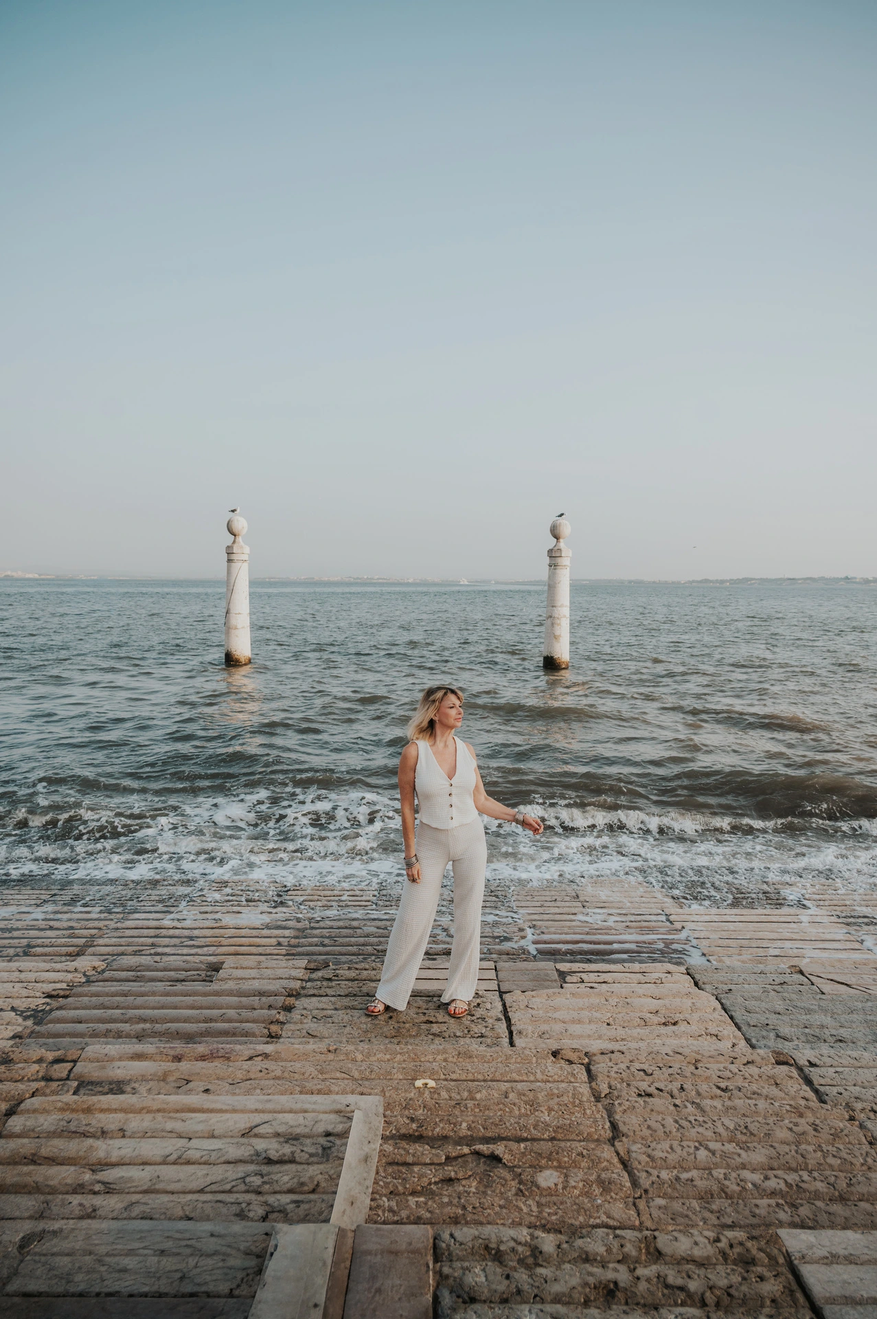 A full-length portrait of the woman on the waterfront steps beside the waves near Praça do Comércio during her solo photoshoot in Lisbon.