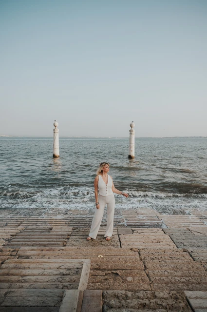 A full-length portrait beside the water | Lisbon solo photoshoot A full-length portrait of the woman on the waterfront steps beside the waves near Praça do Comércio during her solo photoshoot in Lisbon.