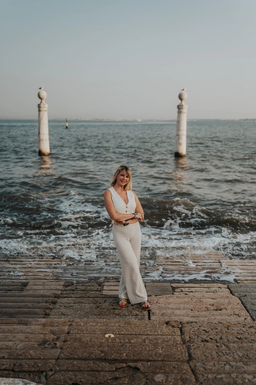 A portrait beside the waterfront waves | Lisbon solo photoshoot The woman standing on the waterfront steps with waves and two stone columns behind her near Praça do Comércio during her solo photoshoot in Lisbon.