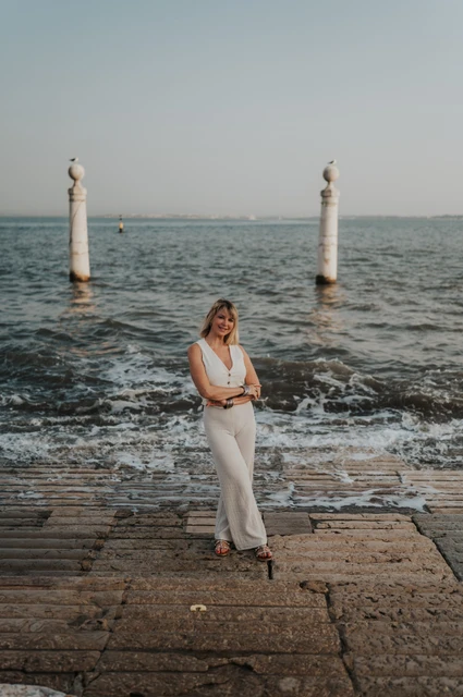 A portrait beside the waterfront waves | Lisbon solo photoshoot The woman standing on the waterfront steps with waves and two stone columns behind her near Praça do Comércio during her solo photoshoot in Lisbon.