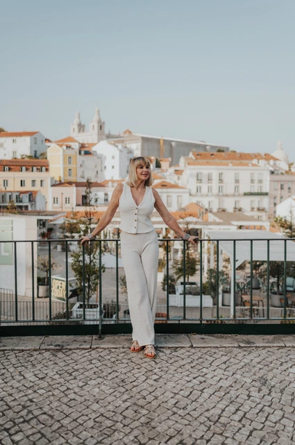A wide portrait above Alfama’s rooftops | Lisbon solo photoshoot The solo traveller leaning against the railing with Alfama’s rooftops behind her at Portas do Sol during her solo photoshoot in Lisbon.